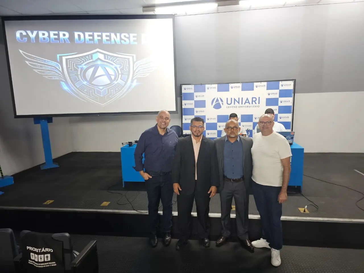 Participantes do Cyber Defense Day 2026 reunidos diante do painel do evento na UniAri, em Fortaleza